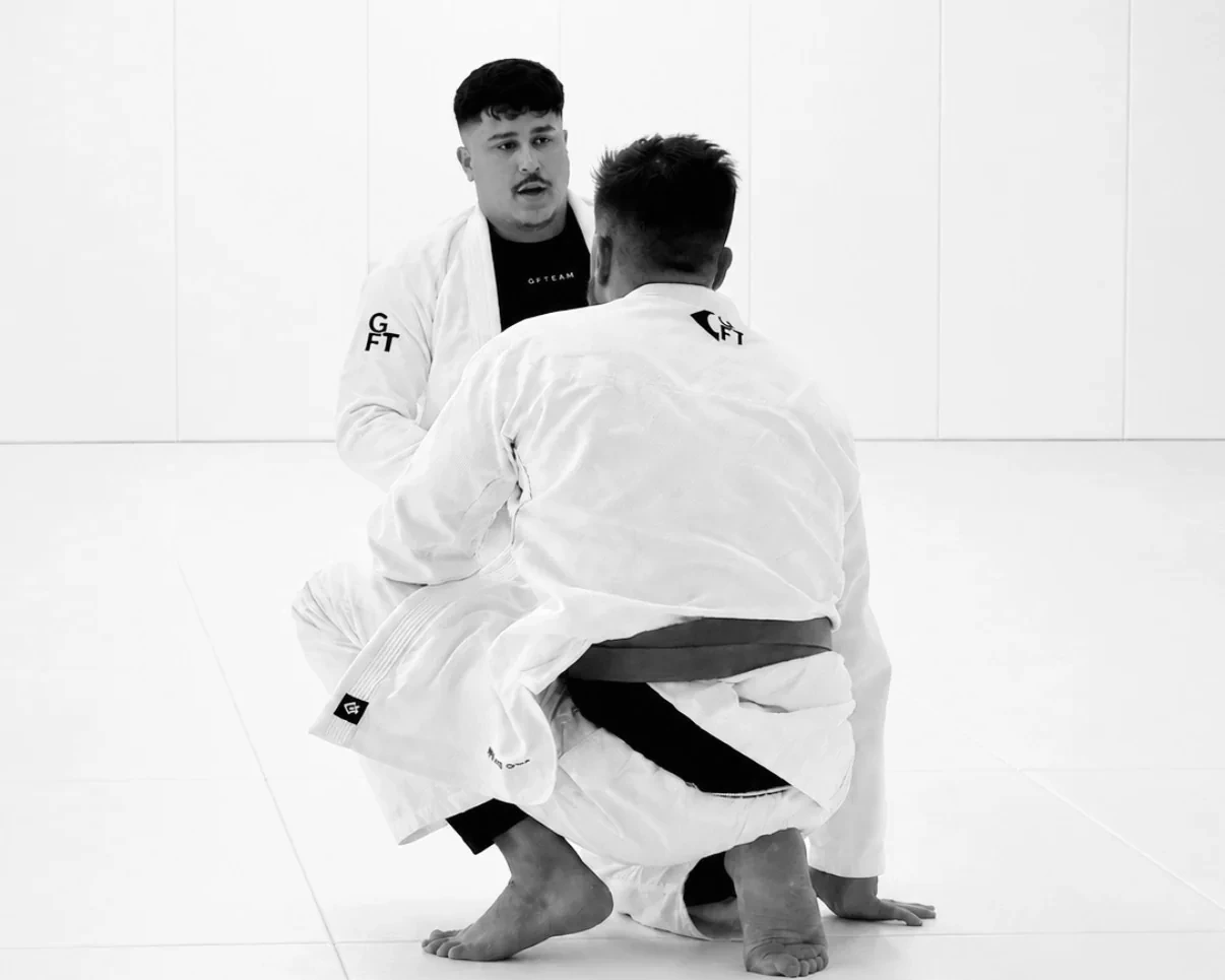 Two GFTEAM APEX students working a grip on the mat, one coaching the other through the detail.